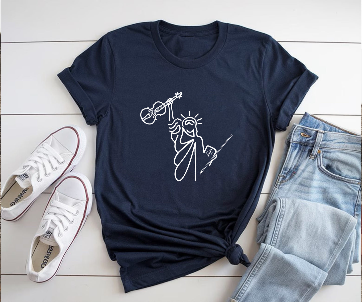 Navy blue t-shirt with a white graphic design on a wooden surface with sneakers and jeans.