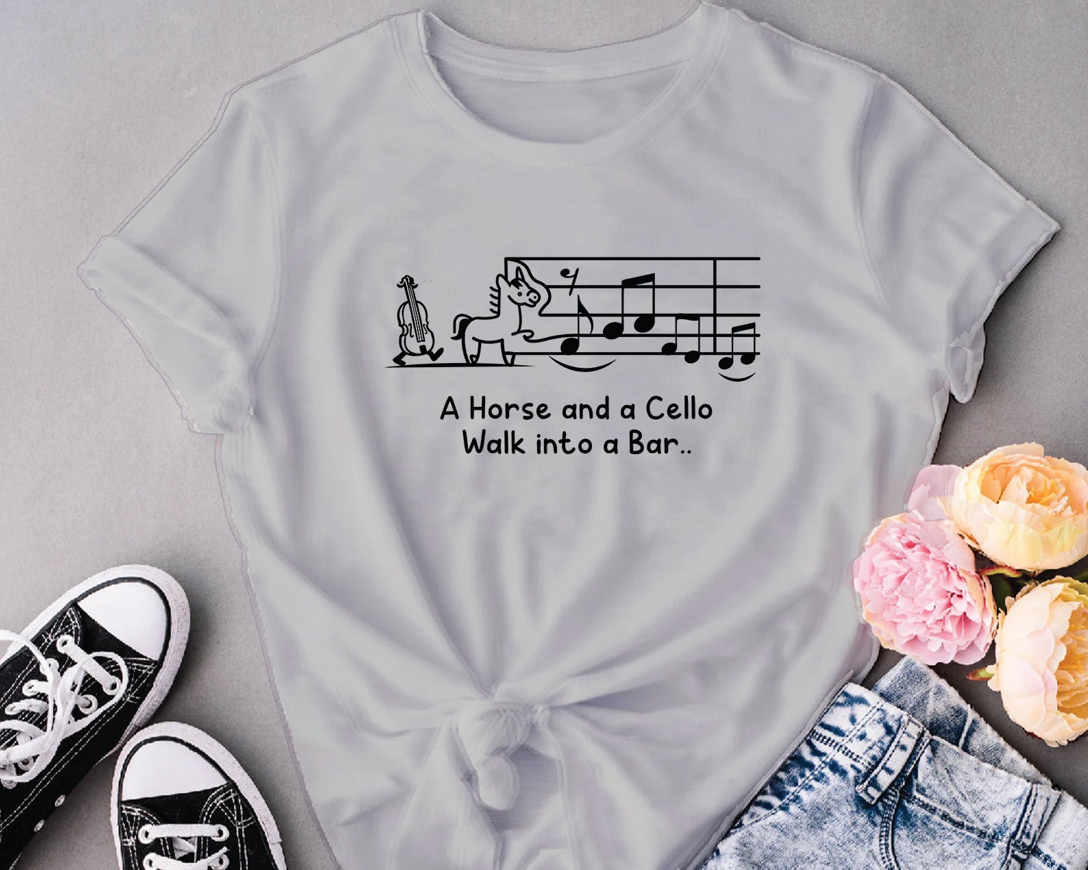 Gray t-shirt with a humorous graphic and text, paired with sneakers and flowers on a gray background