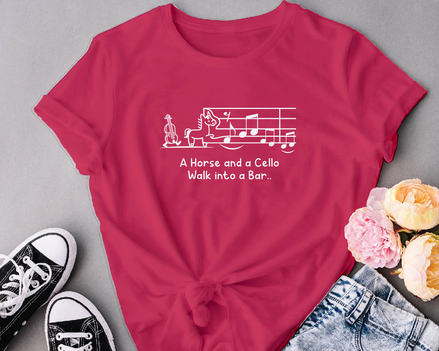 Red t-shirt with a graphic and text, placed on a gray surface with shoes and flowers.