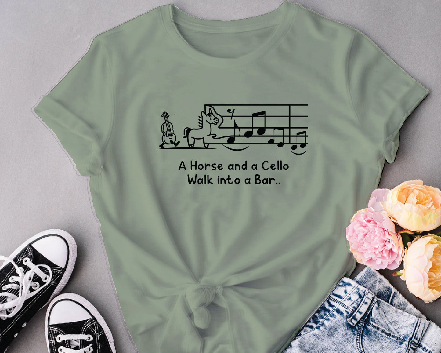 Green t-shirt with a humorous design and text, placed on a gray surface with sneakers and flowers.