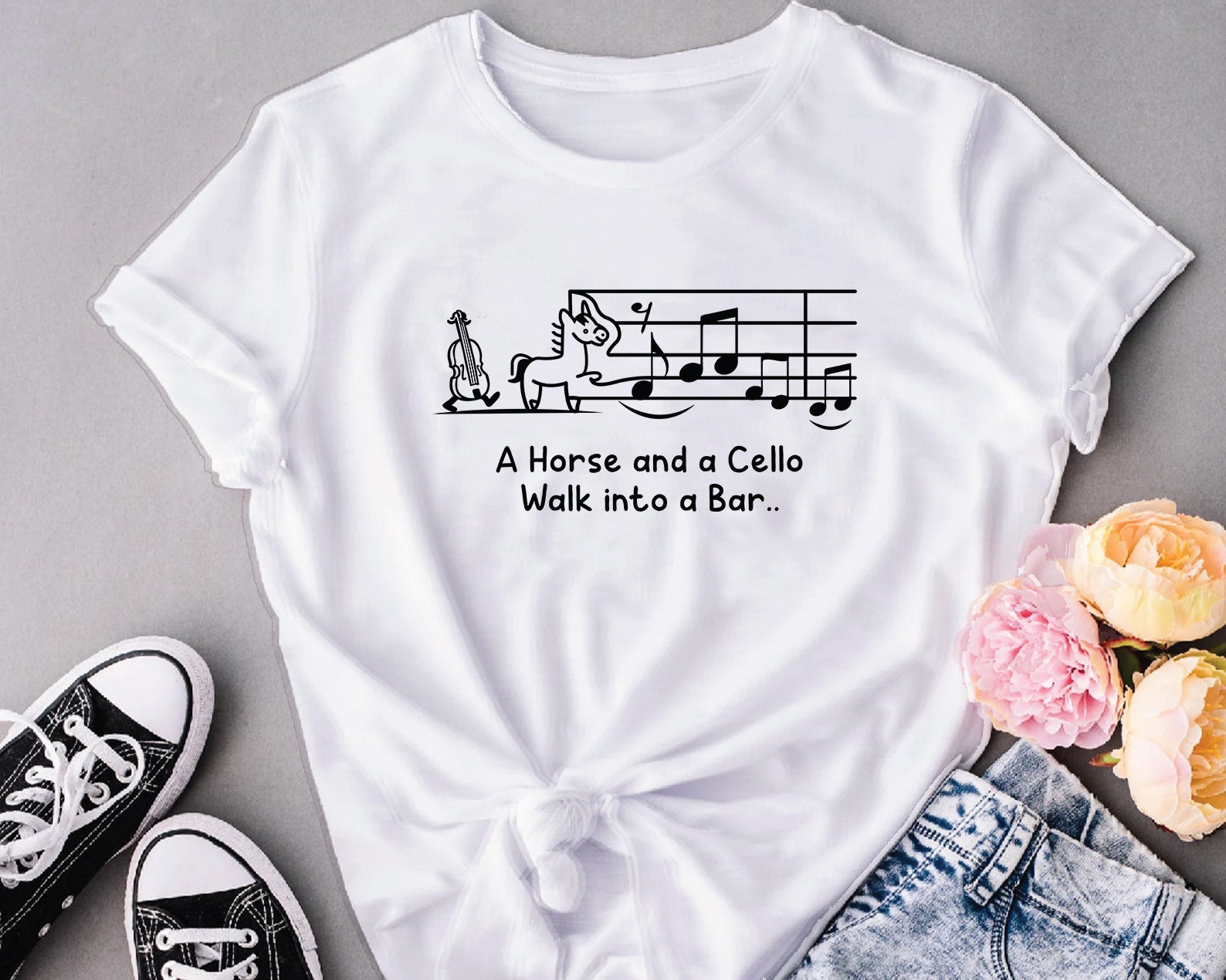 White t-shirt with humorous design and text, paired with sneakers and flowers on a gray background